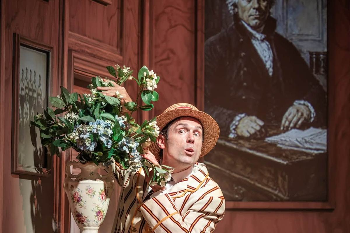 Sam Harrison in a straw boater beside a vase of flowers in Jeeves Takes Charge at the Charing Cross Theatre