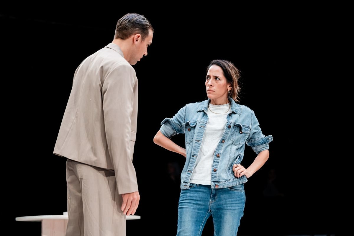 A man in a pale suit and a woman in a denim jacket on stage in Memoriam A man in a pale suit and a woman in a denim jacket on stage in Memoriam