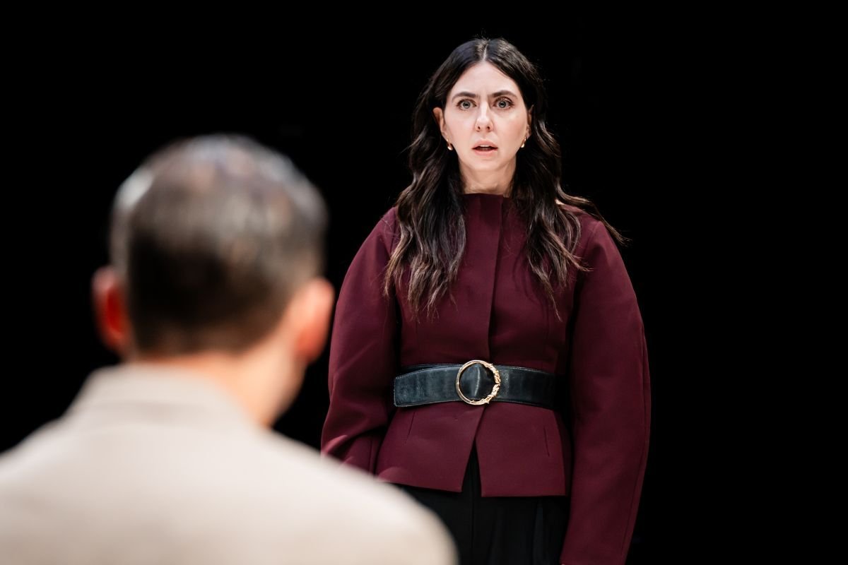 A young woman in a burgundy top faces a man seen from behind in Memoriam A young woman in a burgundy top faces a man seen from behind in Memoriam