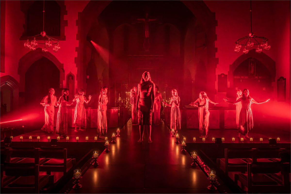 The Women of Canterbury in a red-lit church nave in Murder in the Cathedral at St John the Divine, Richmond. Photo by Marc Brenner