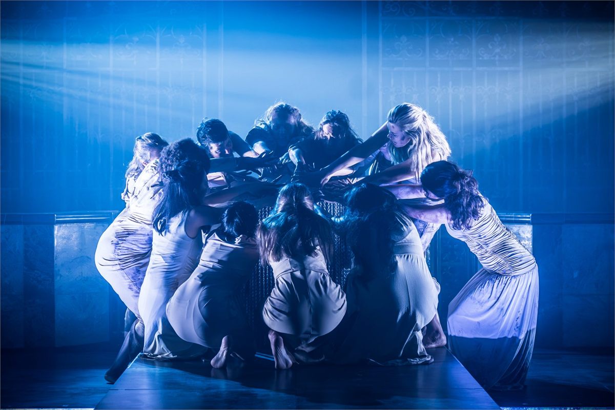 The Women of Canterbury huddled together under blue light in Murder in the Cathedral. Photo by Marc Brenner