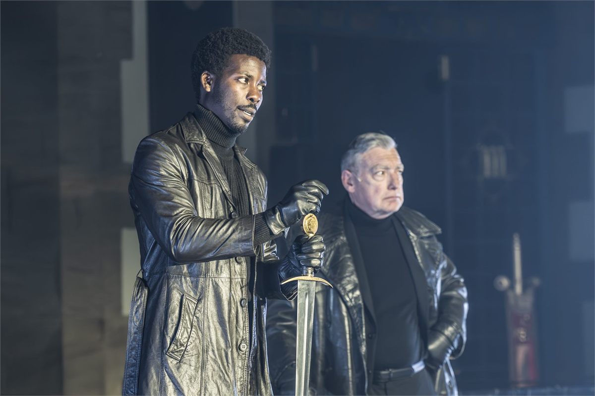 Two of the knights in black leather coats, one holding a sword, in Murder in the Cathedral. Photo by Marc Brenner