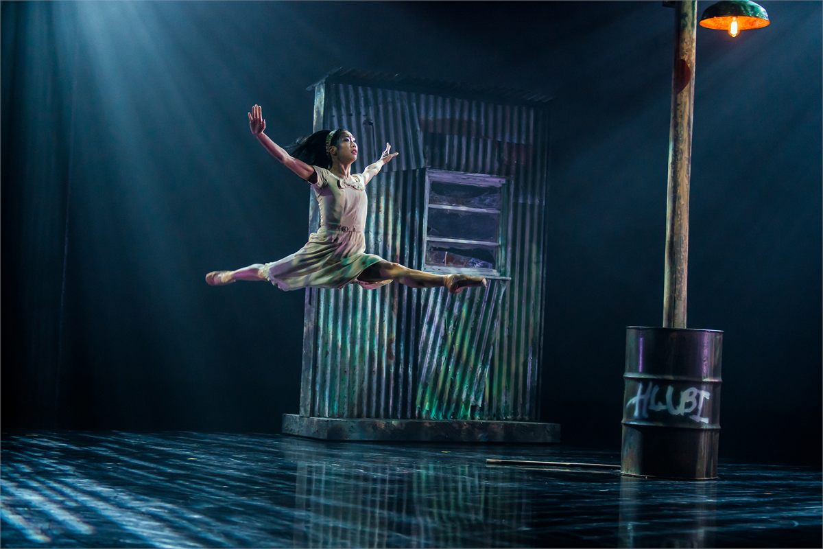 Sarah Chun leaps beside a township shack in Fools for Northern Ballet. Photo by Emily Nuttall