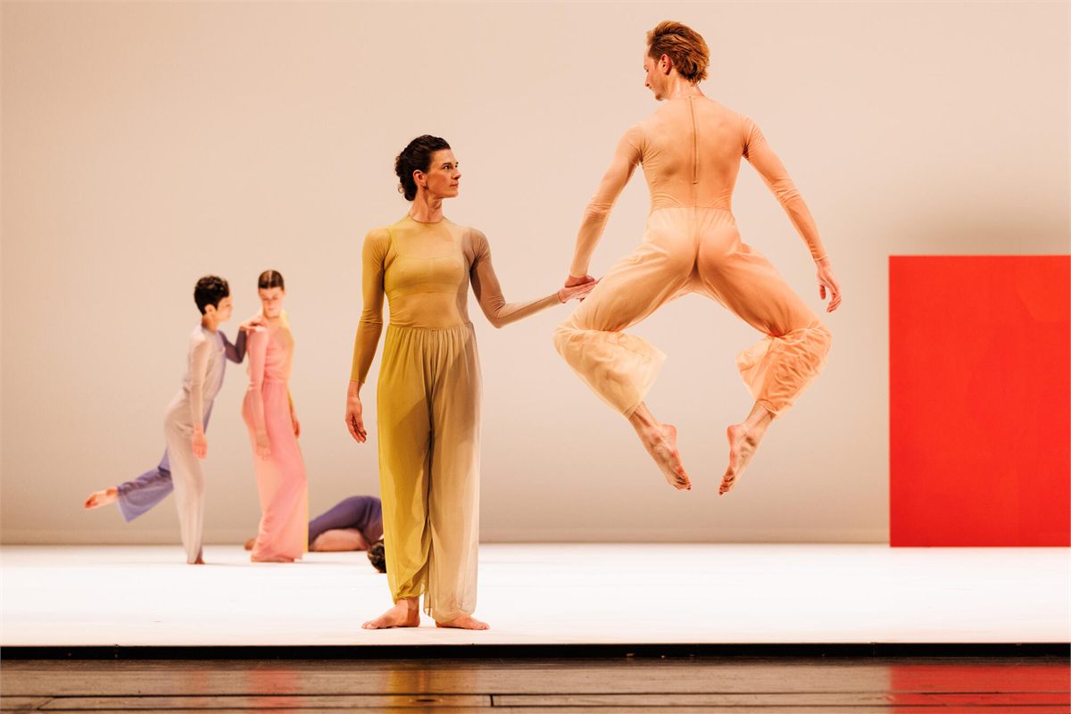 A dancer of Pam Tanowitz Dance leaps beside a colleague in front of a red canvas in Pastoral. Photo by Maria Baranova