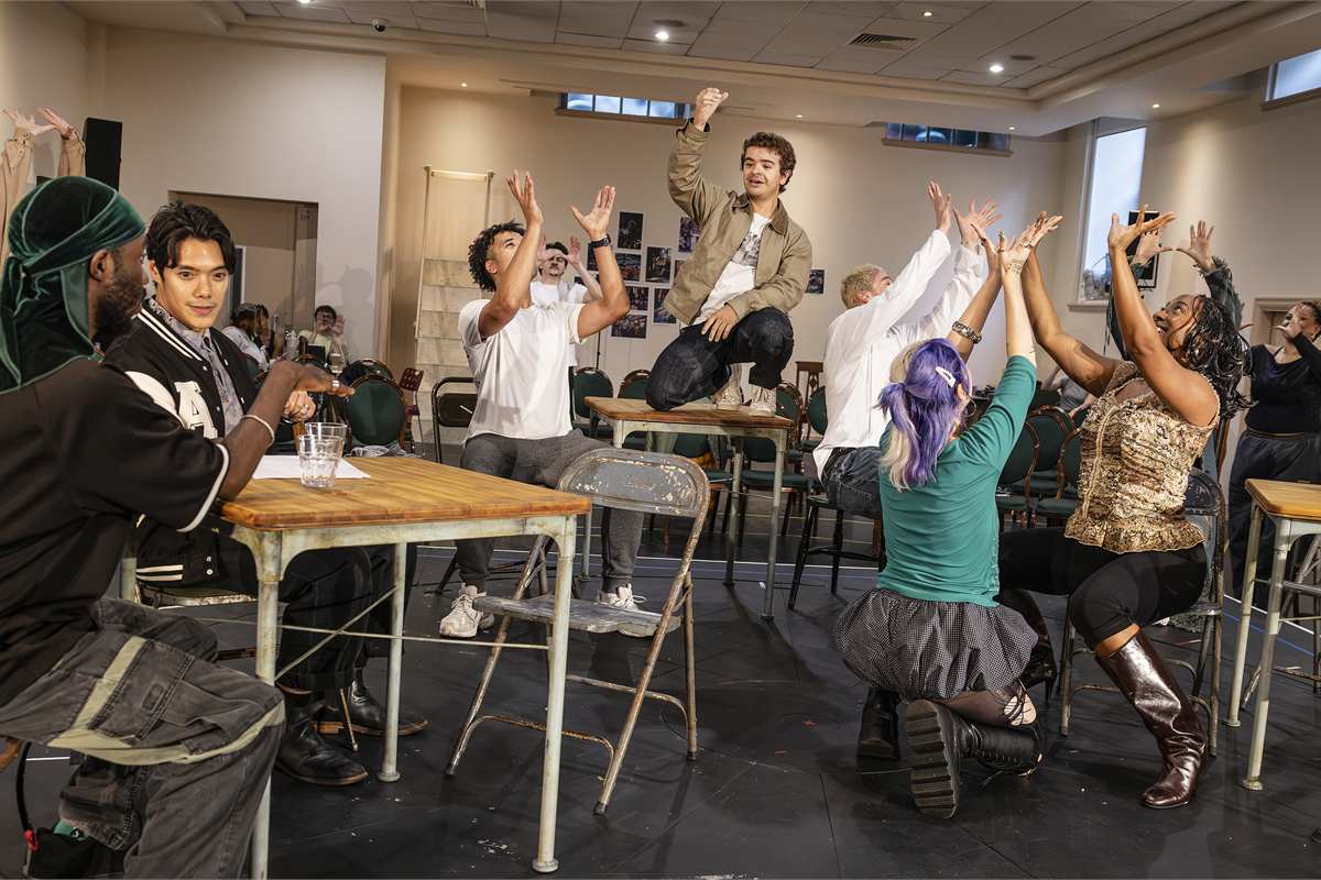 The company of Rent in rehearsal, with Gaten Matarazzo standing on a table. Photo by Pamela Raith