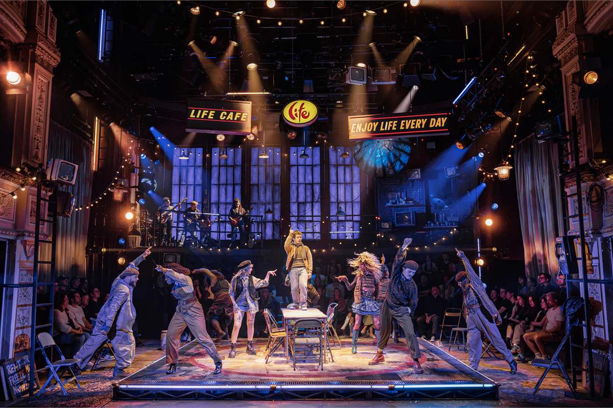 The company of Rent on stage at the Life Cafe, with Gaten Matarazzo standing on the table at the centre. Photo by Pamela Raith