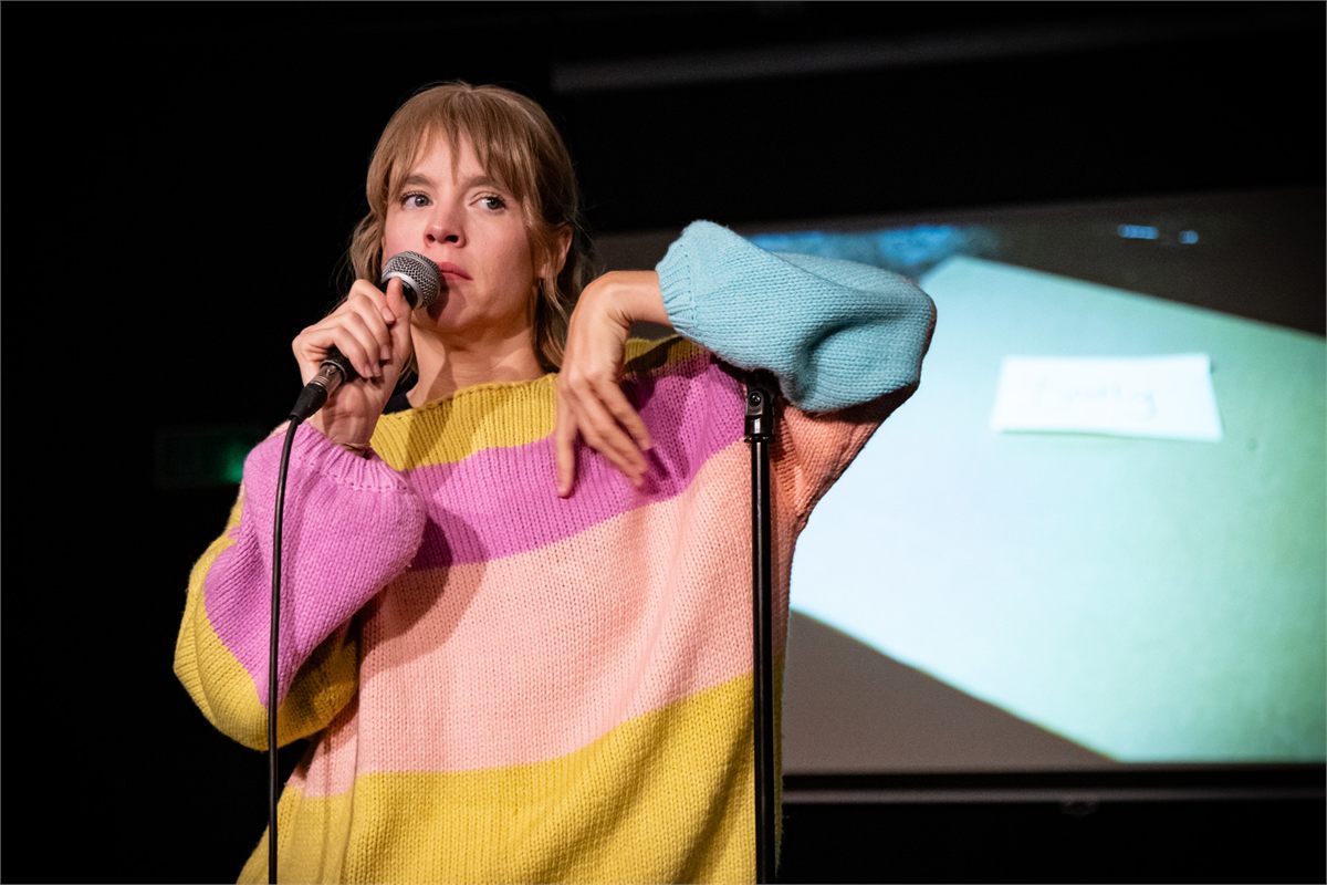 Jessica Clark at a microphone stand in a striped jumper in Dolly at the Omnibus Theatre