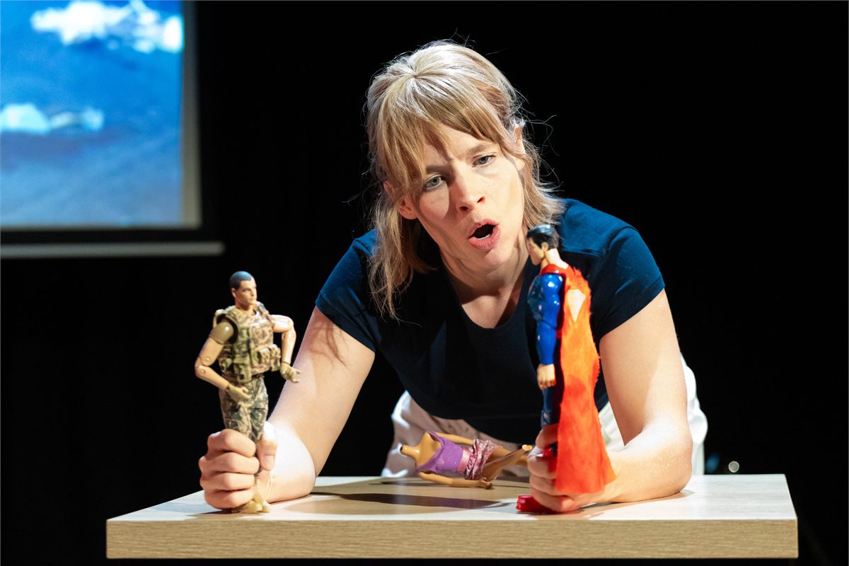 Jessica Clark holding two action figures at a table in Dolly at the Omnibus Theatre
