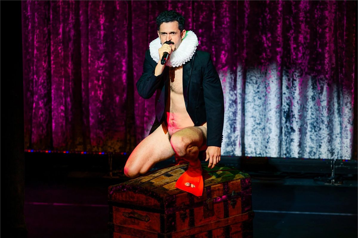 Damien Warren-Smith as Garry Starr, in a ruff and tailcoat, kneeling on a trunk in Garry Starr: Classic Penguins at The Other Palace