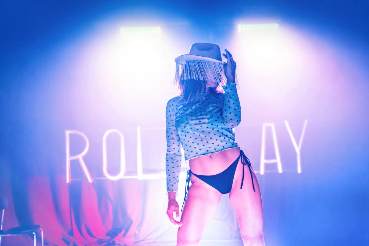 Hannah Reilly in a fringed cowboy hat poses under pink and blue light in Roleplay at Soho Theatre Hannah Reilly in a fringed cowboy hat poses under pink and blue light in Roleplay at Soho Theatre