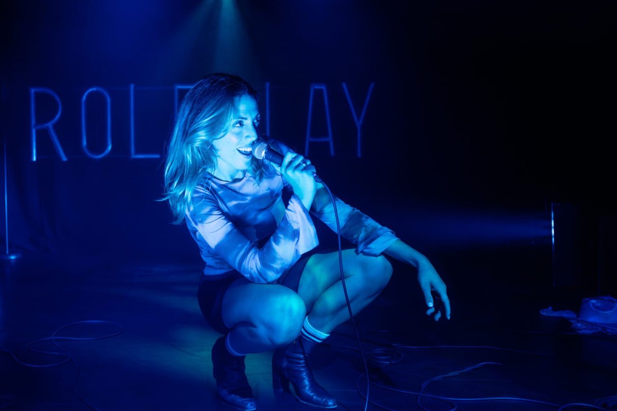 Hannah Reilly crouches with a microphone in blue light in Roleplay Hannah Reilly crouches with a microphone in blue light in Roleplay