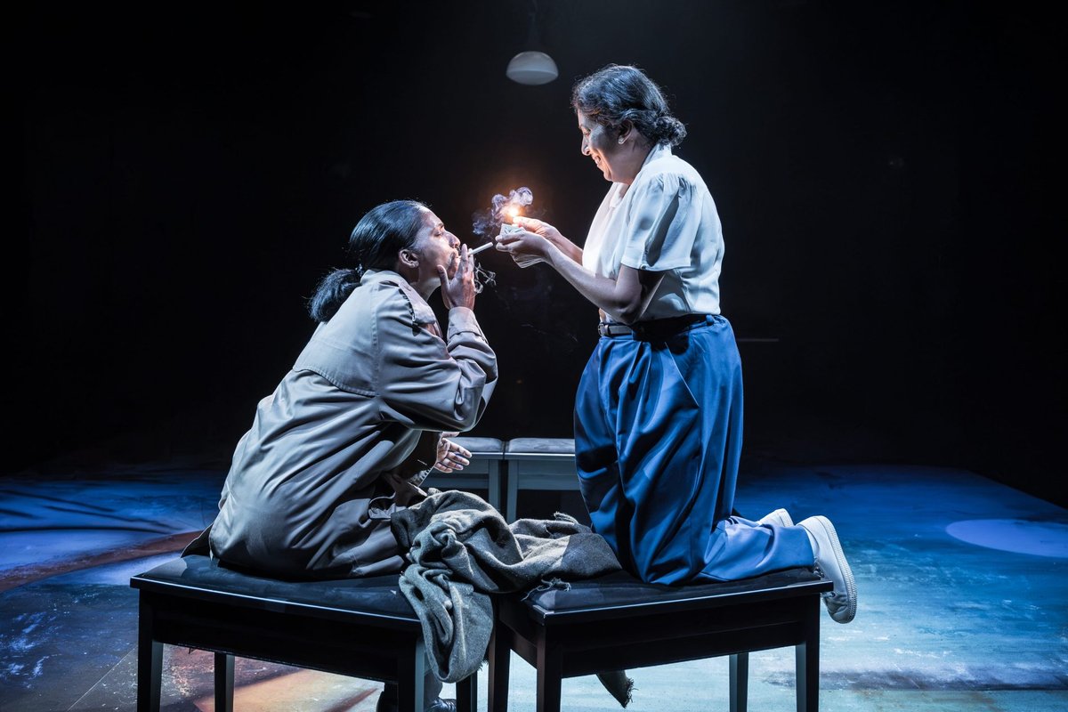 Two members of the all-female company share a light in a small and quiet light. Photo by Marc Brenner