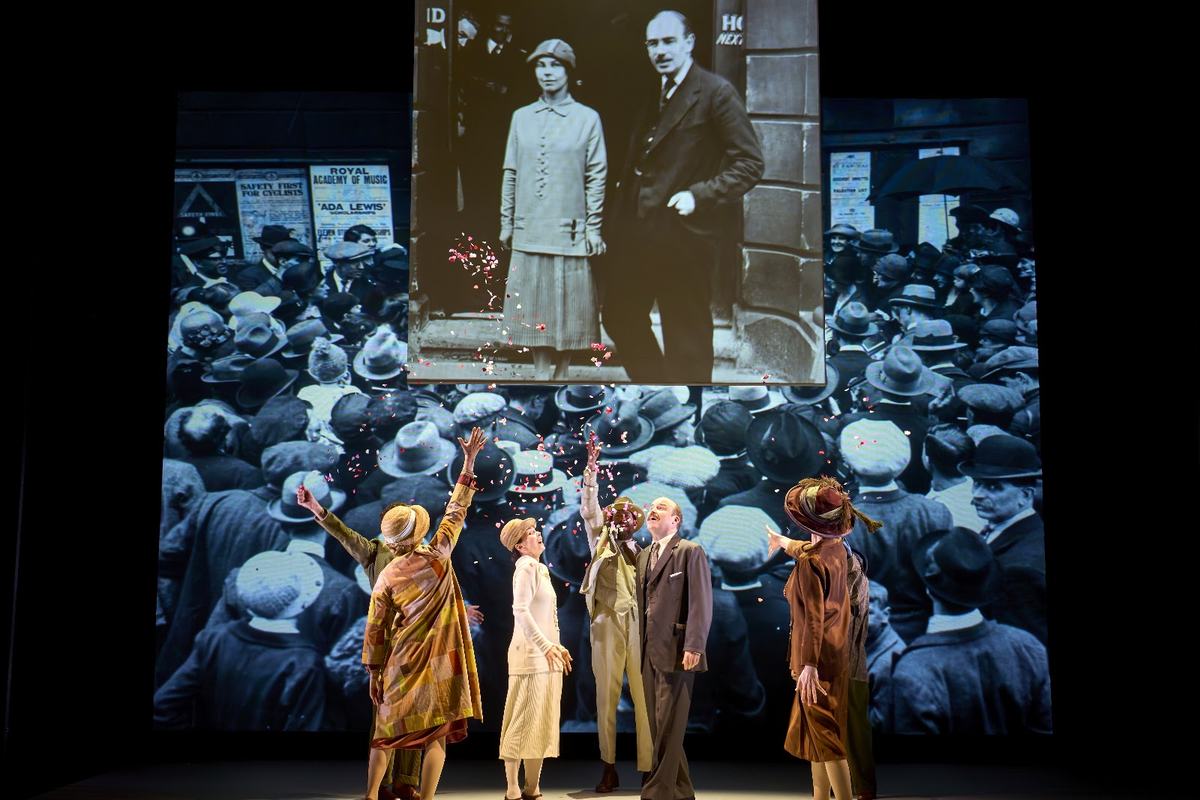 The company of The Standard of Living against a projected archive crowd scene. Photo by Manuel Harlan