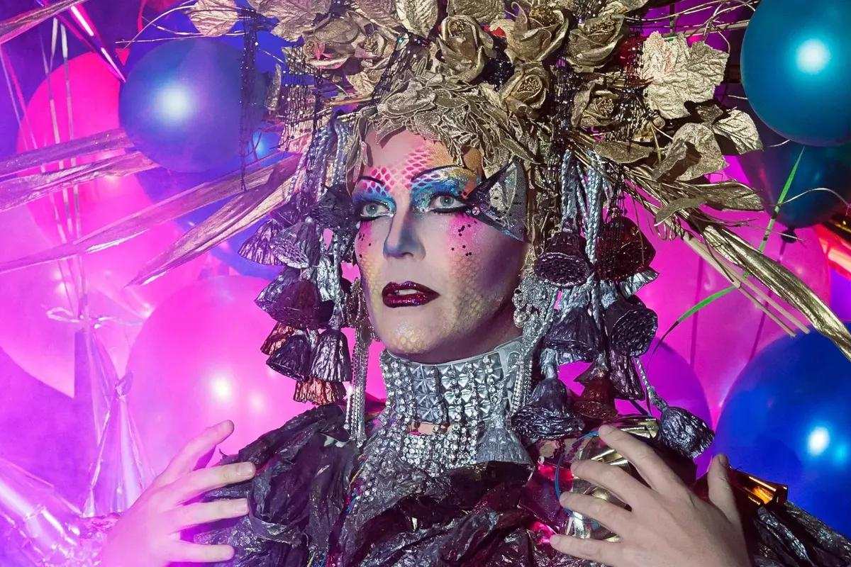 Taylor Mac in a gold headdress surrounded by balloons. Photo by Little Fang