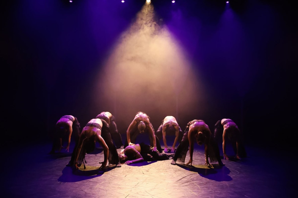 The dancers of Tellus bent low in a circle beneath a beam of light on a purple-lit stage